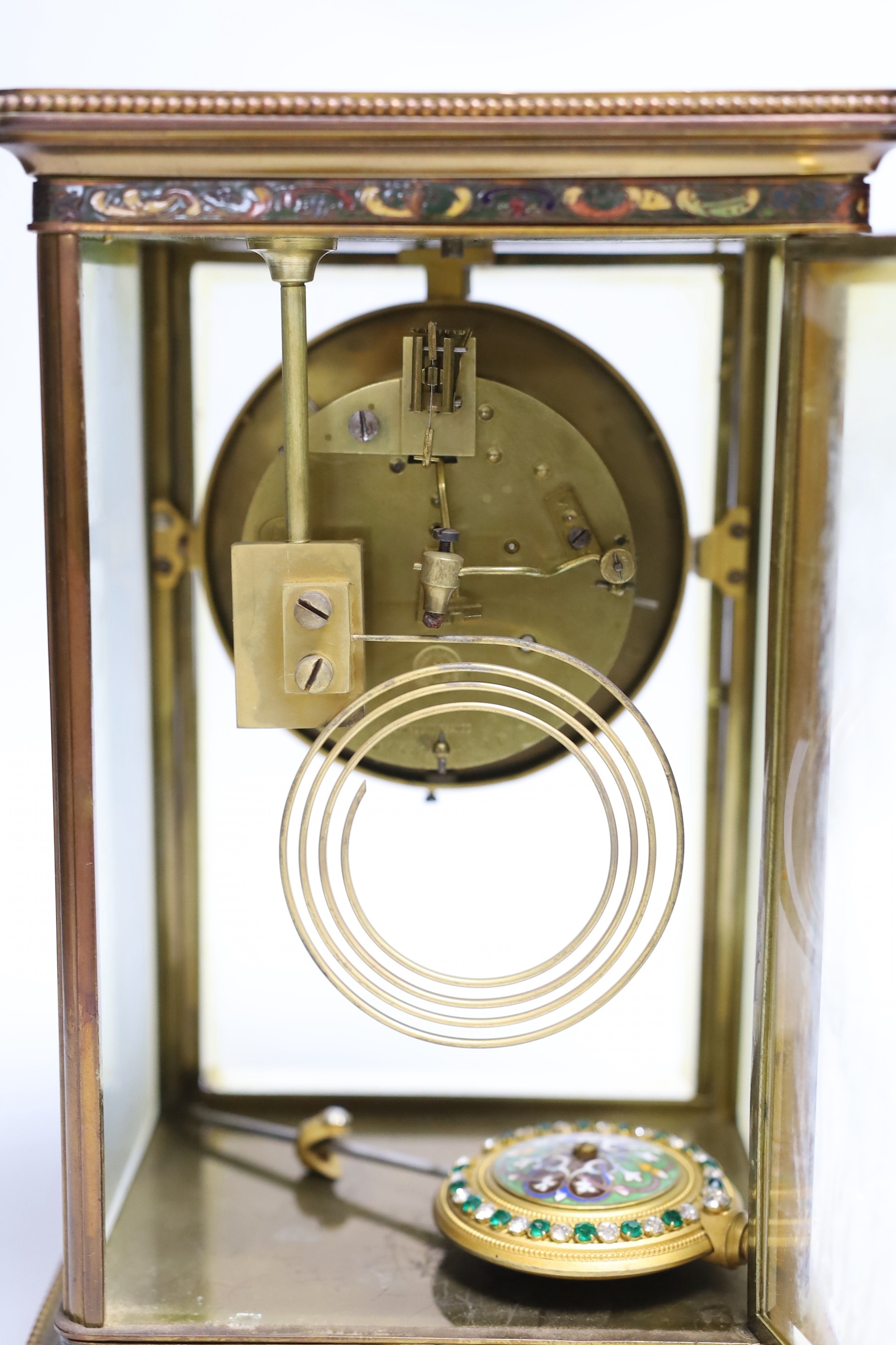 An early 20th century four glass brass and champleve enamel clock, with decorative enamelled and paste dial and pendulum, 7cms wide, 28cms high